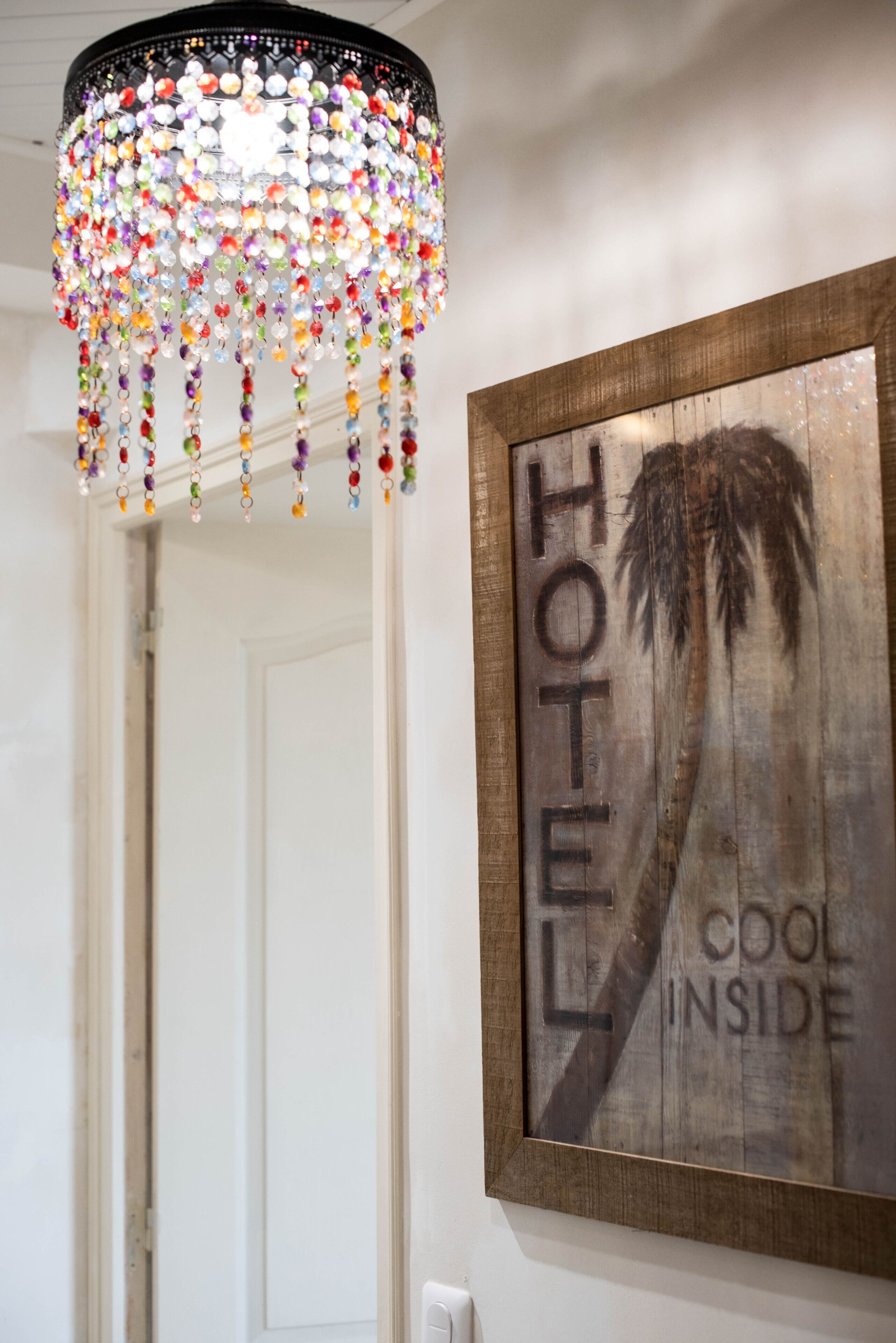 Interior de um hotel com um lustre decorativo e uma placa emoldurada com a inscrição 'HOTEL COOL INSIDE'.