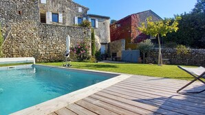 A swimming pool with a wooden deck, stone walls, and a grassy yard.