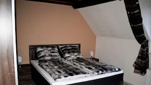Ein Schlafzimmer mit Bett, Nachttisch, Lampe und Vorhang.