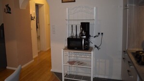 Eine kompakte Küche mit einer Mikrowelle auf einem Regal, einer Kaffeemaschine und einem kleinen Essbereich mit einem Stuhl.
