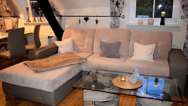 Ein modernes Wohnzimmer mit einer Eckcouch, einem Glastisch und einem Essbereich mit Tisch und Stühlen.