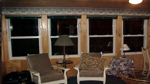 A cozy room with a large window, a chair, a small table, and a lamp. - 4 Season Secluded Lakefront Home near Ski Mountains  (Mt Holly)