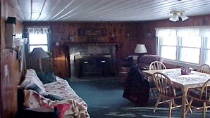A cozy cabin interior with a wooden floor, a sofa, a dining table with chairs, a lamp, and a fireplace. - 4 Season Secluded Lakefront Home near Ski Mountains  (Mt Holly)