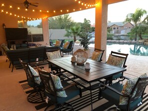 An outdoor patio with a dining table, chairs, and string lights. - Resort Living! Quiet Lakefront Home. Pool, large shaded patio, fishing, sleeps 9 (Chandler)