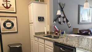 A kitchen with white cabinets, a stainless steel dishwasher, a granite countertop, and a red patterned rug. -  Village by the Beach!Townhome Walking distance to the BEACH, Heated Resort Pool (Corpus Christi)