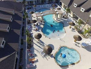Ein Resort mit zwei Schwimmbecken, Liegestühlen, Sonnenschirmen und einer kleinen Wasserrutsche.