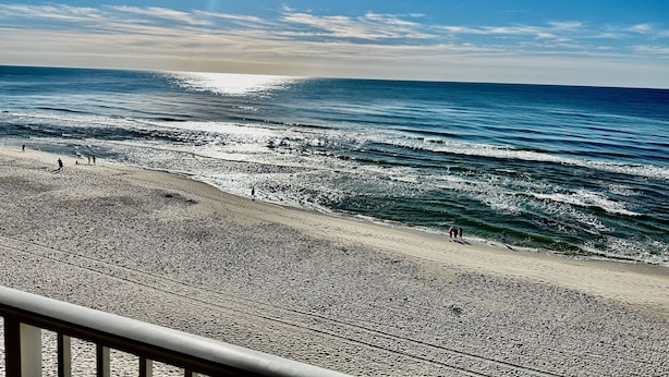 Une plage avec des vagues, un ciel dégagé et un soleil.