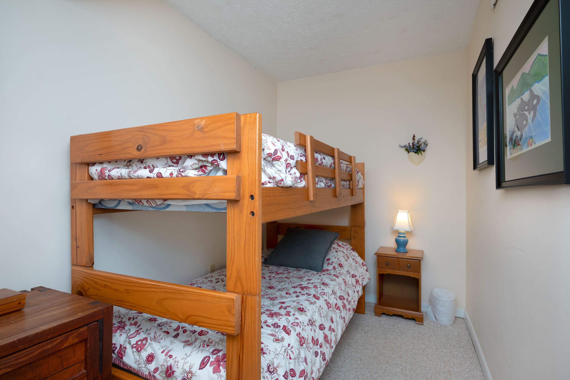 A bunk bed with floral bedding, a bedside table with a lamp, and a small nightstand.