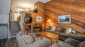 Una sala de estar acogedora con chimenea, paredes de madera y televisor.