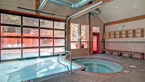 Una piscina con cerramiento de vidrio, vigas de madera y una zona de bancos.