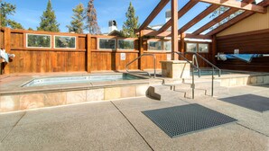 Una cabaña de madera con jacuzzi, mobiliario exterior y vista a los árboles.