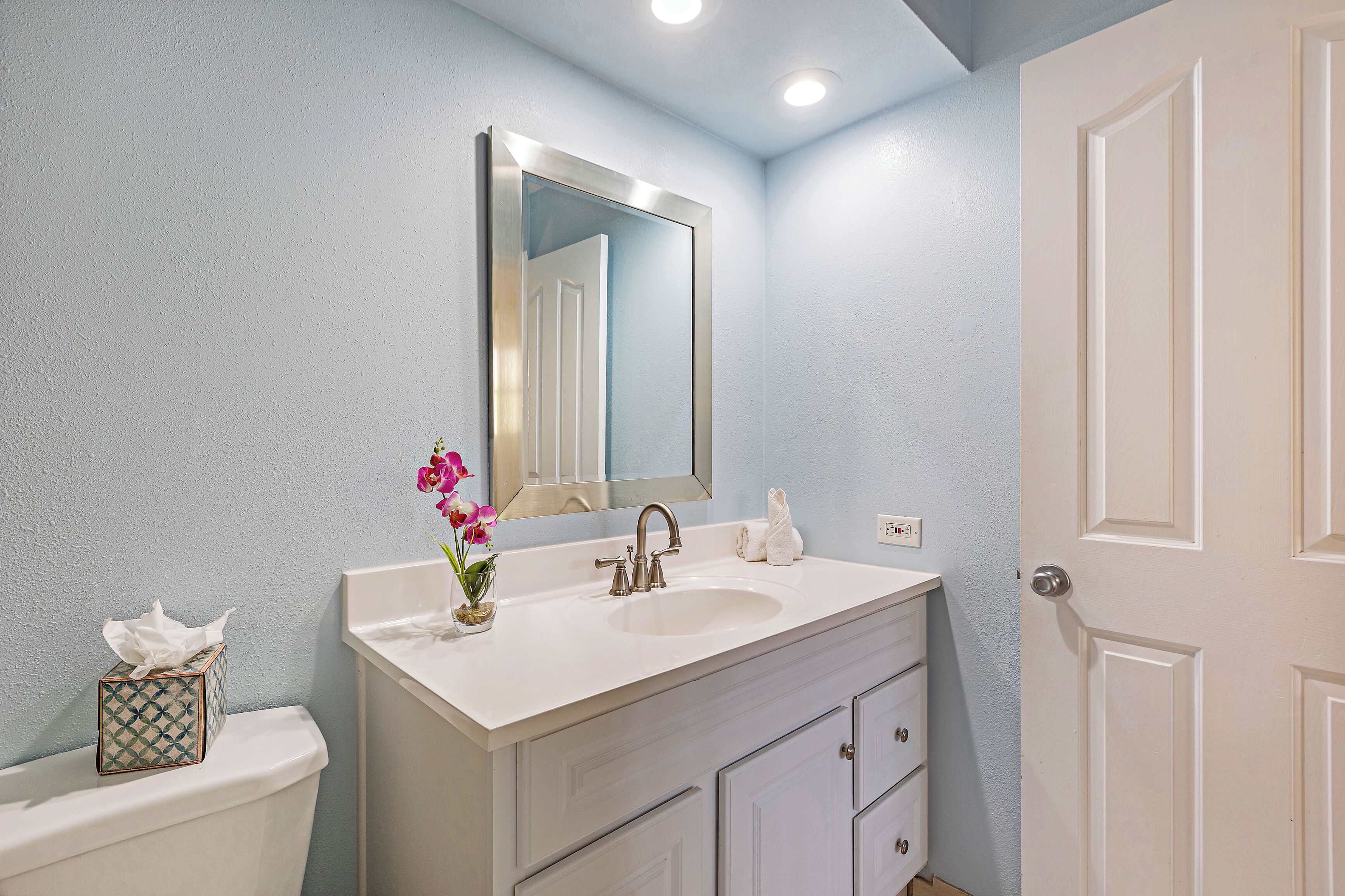 A bathroom with a white sink, a mirror, a toilet, and a door.