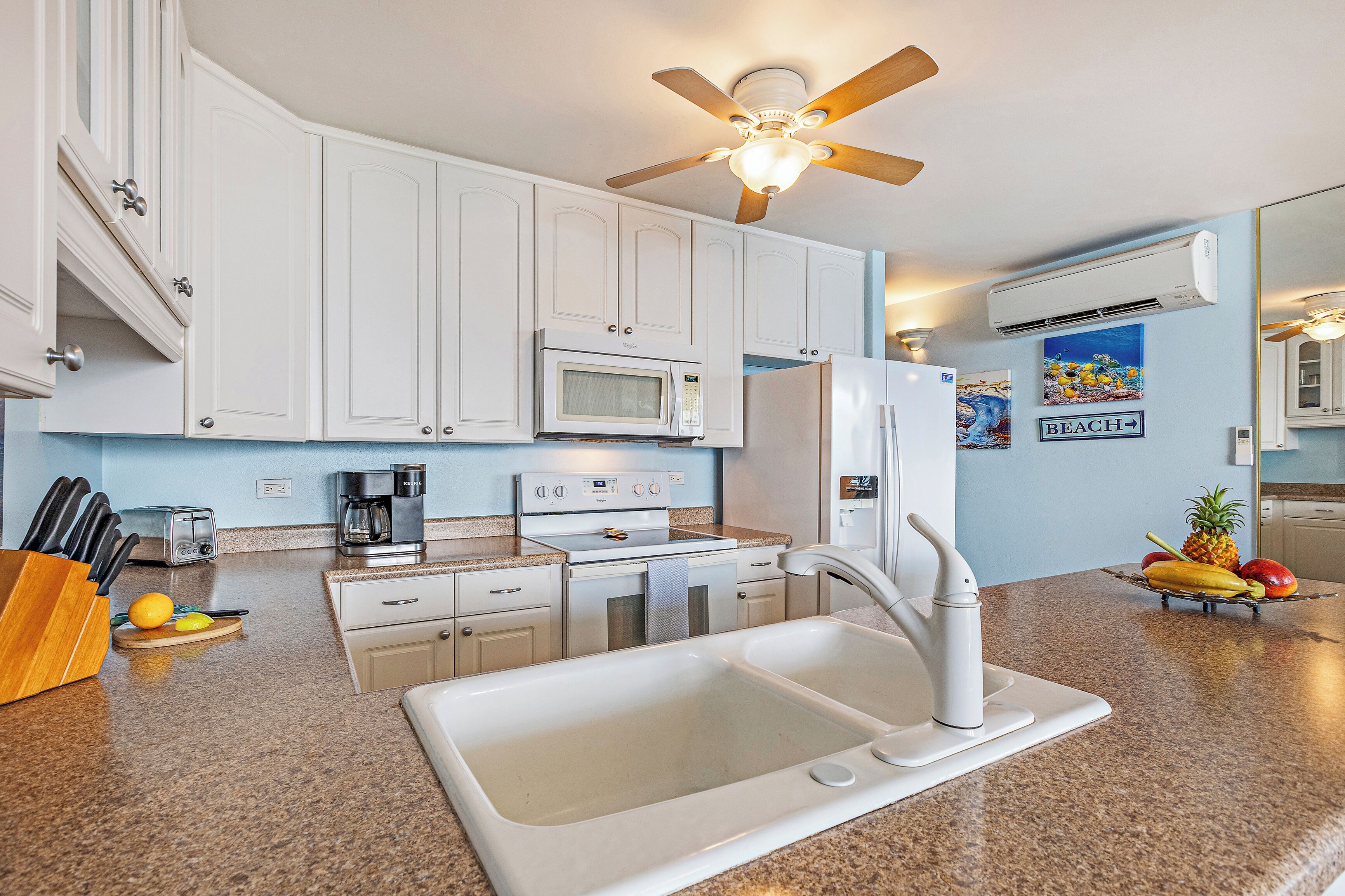 Una cocina moderna con armarios blancos, microondas, refrigerador, pileta y ventilador de techo.