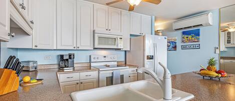 Una cocina moderna con armarios blancos, microondas, refrigerador, pileta y ventilador de techo.