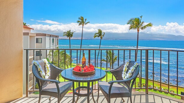 Ein Balkon mit Tisch für zwei Personen, der auf einen Strand mit Palmen und den Ozean blickt.