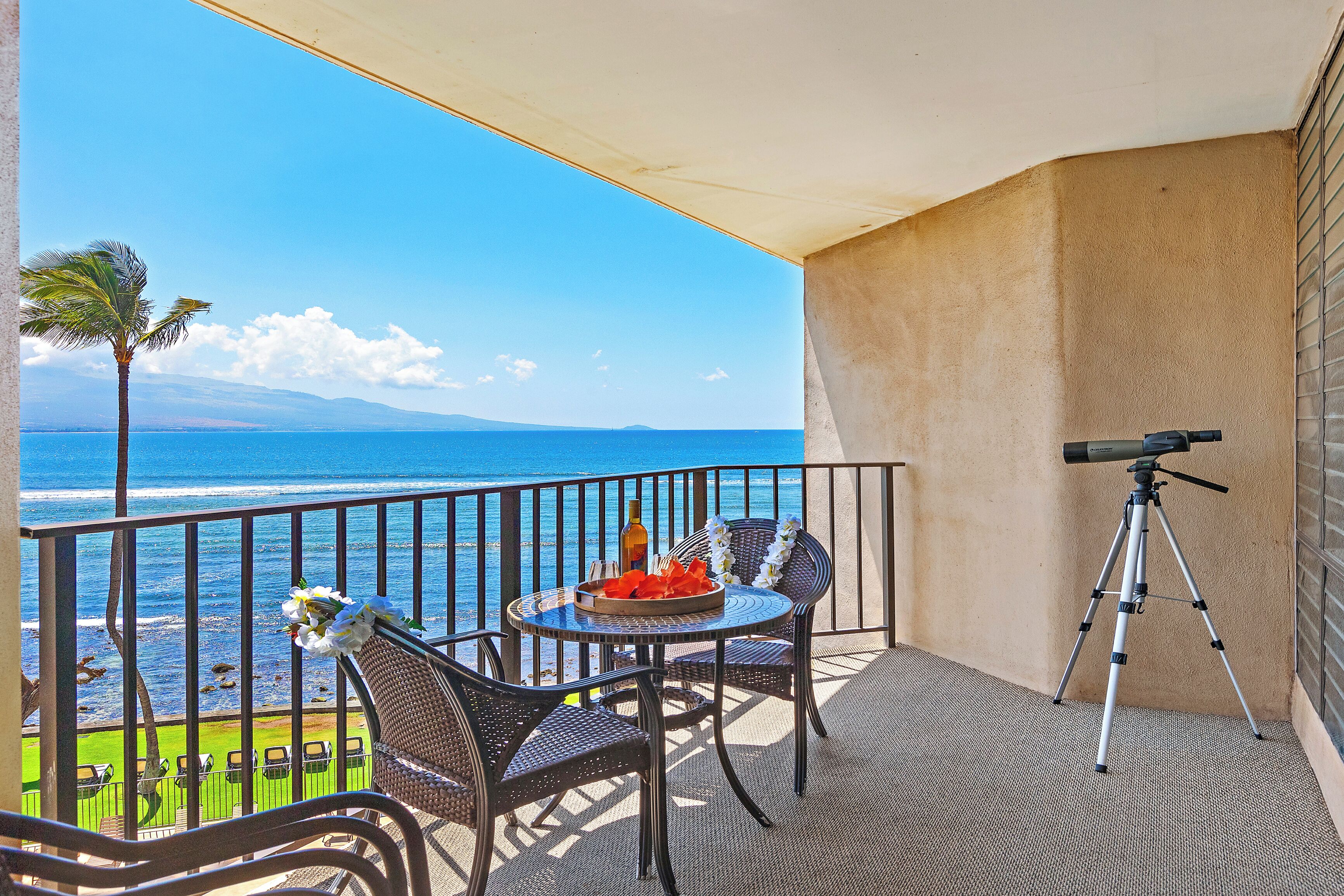 Ein Balkon mit Blick auf den Ozean, ein Teleskop, Korbstühle und ein Tisch mit Blumen und einer Flasche.