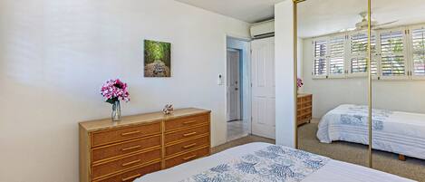 Une chambre à coucher avec un lit, une commode, un miroir et une fenêtre avec des stores.