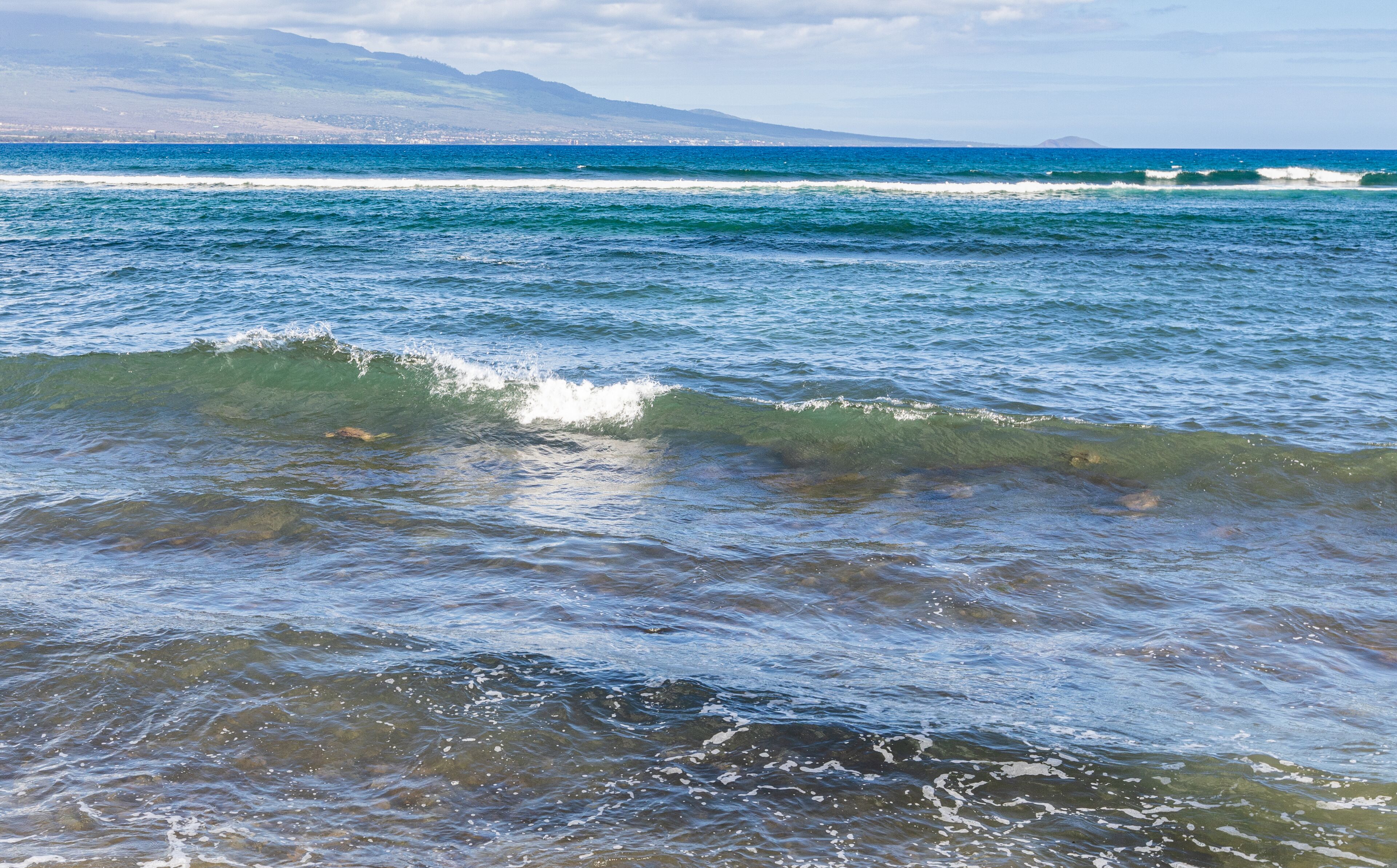 A coastal view with waves and a distant mountain range.
