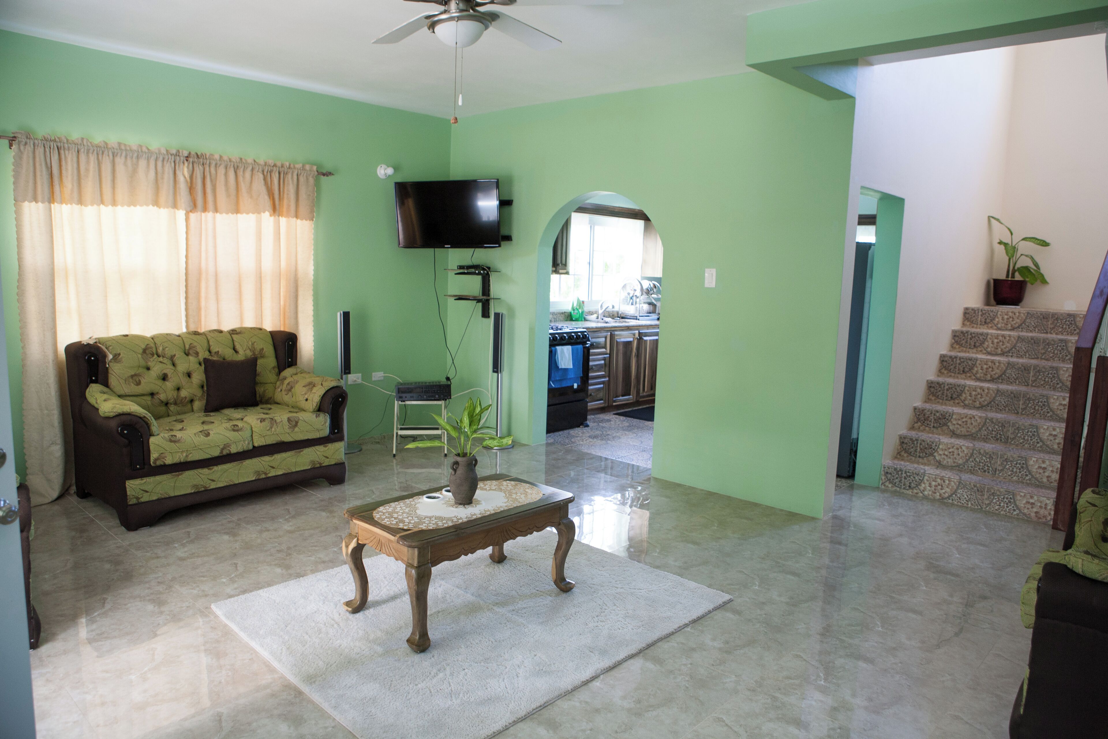 A living room with a sofa, a coffee table with a vase, a television, and a staircase leading to a kitchen.
