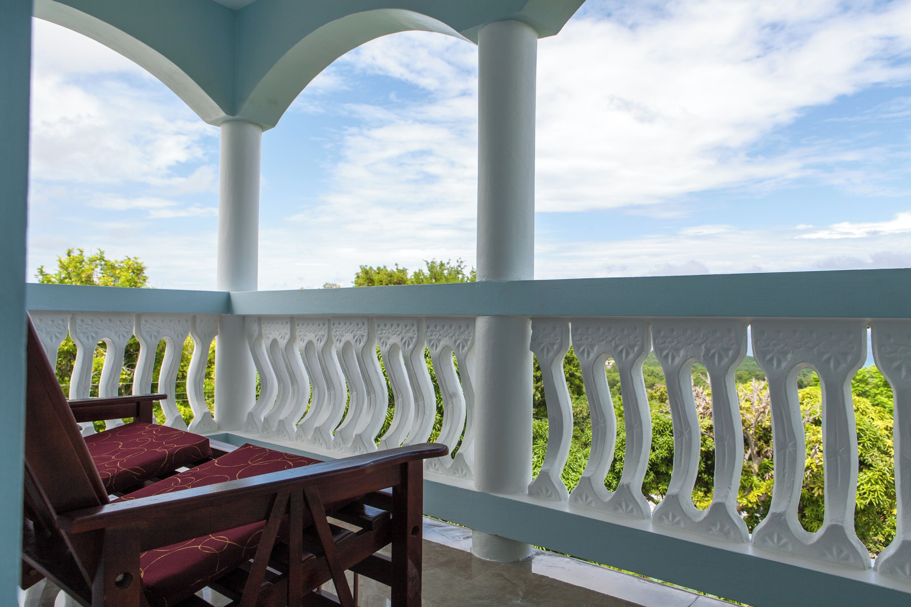 A covered outdoor seating area with a white balustrade and a view of greenery.
