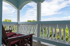 A covered outdoor seating area with a white balustrade and a view of greenery.