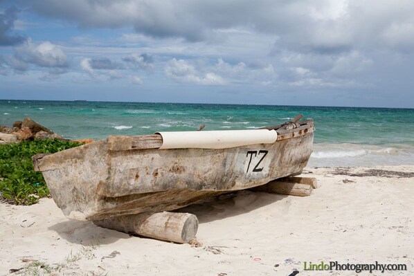 A weathered boat with the number TZ on a sandy beach with the ocean in the background.