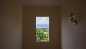 Ein Zimmer mit Fenster und Blick auf eine Küstenlandschaft, einer Wandleuchte und einer schlichten Wand.
