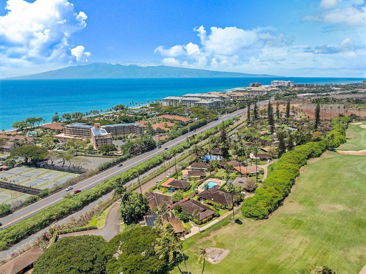 Una vista aerea di un resort costiero con diversi edifici, una strada e un campo da golf.