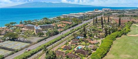 Una vista aerea di un resort costiero con diversi edifici, una strada e un campo da golf.