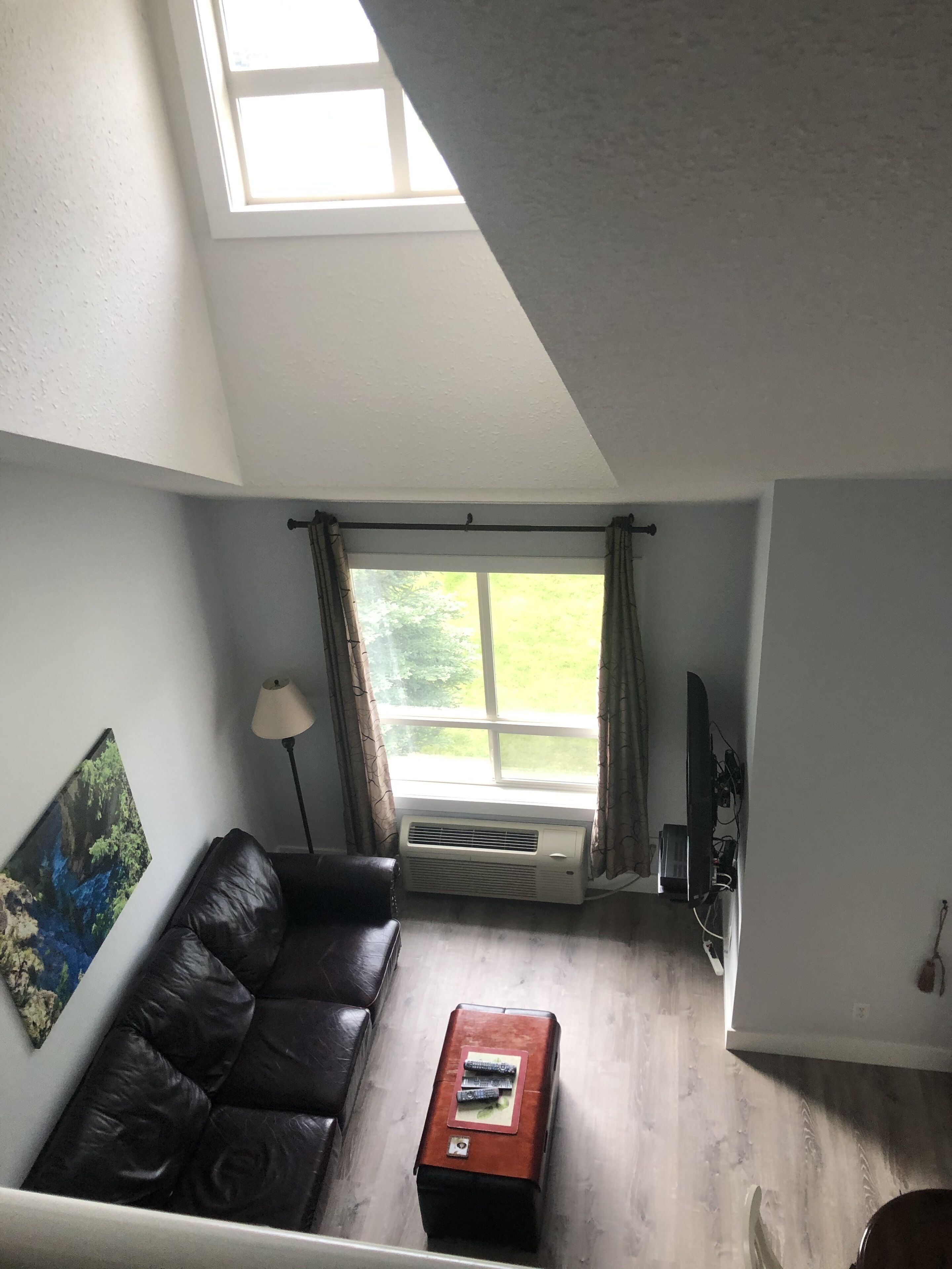 Una sala de estar con un sofá de cuero marrón, una mesa de centro de madera, un televisor de pantalla plana y una ventana con cortinas.