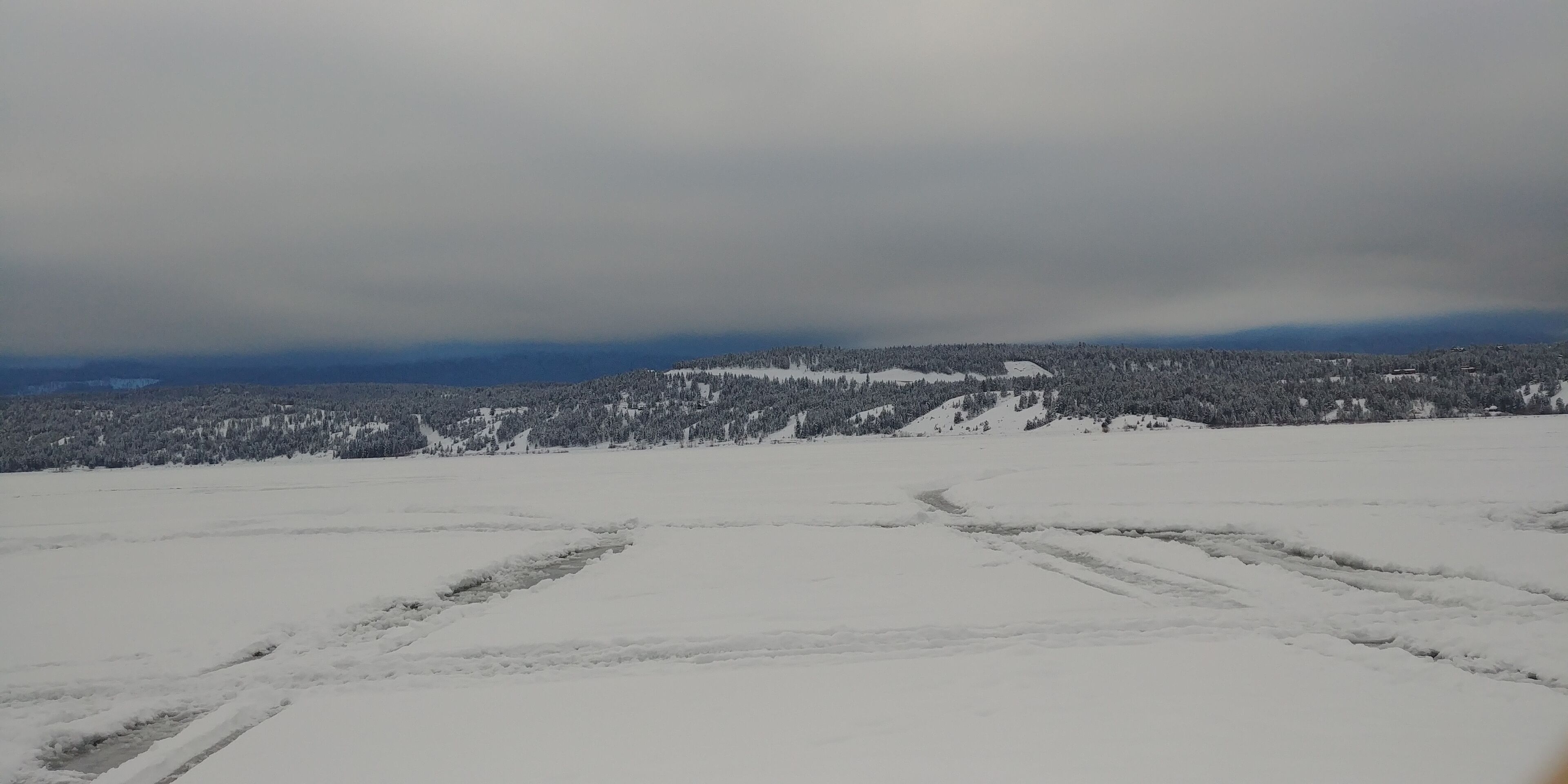 A snow-covered landscape with a flat terrain and distant trees.