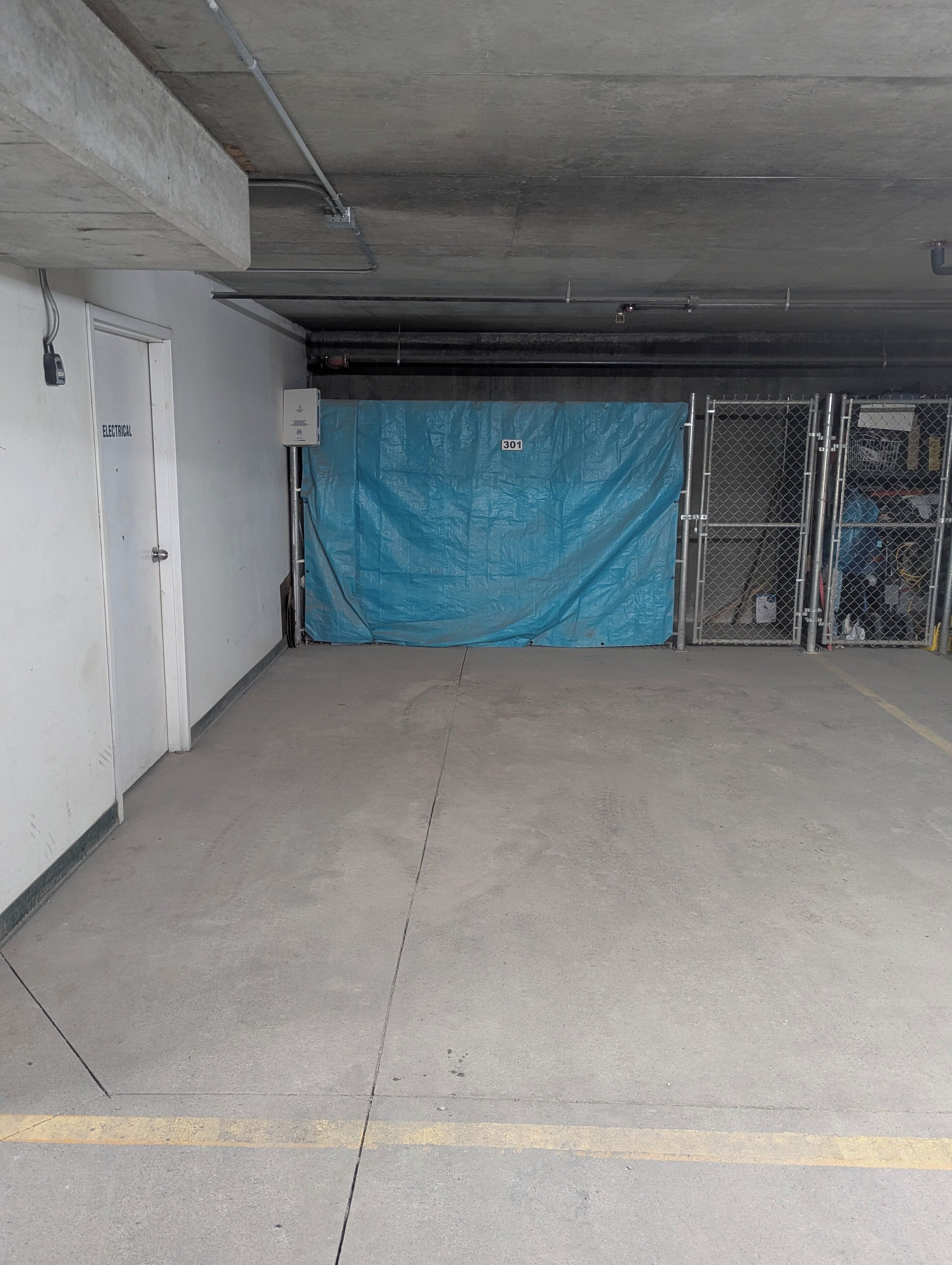 A parking garage with a concrete floor, a blue tarp covering an area, and a chain-link fence.