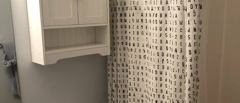 A bathroom with a toilet, a sink, a cabinet above the toilet, and a shower curtain with letters.