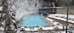 A snow-covered outdoor pool area with a building in the background. - Mountain Views, Pool, Hot Tub! 1500 sqft 2BR + Loft, Penthouse (Radium Hot Springs)