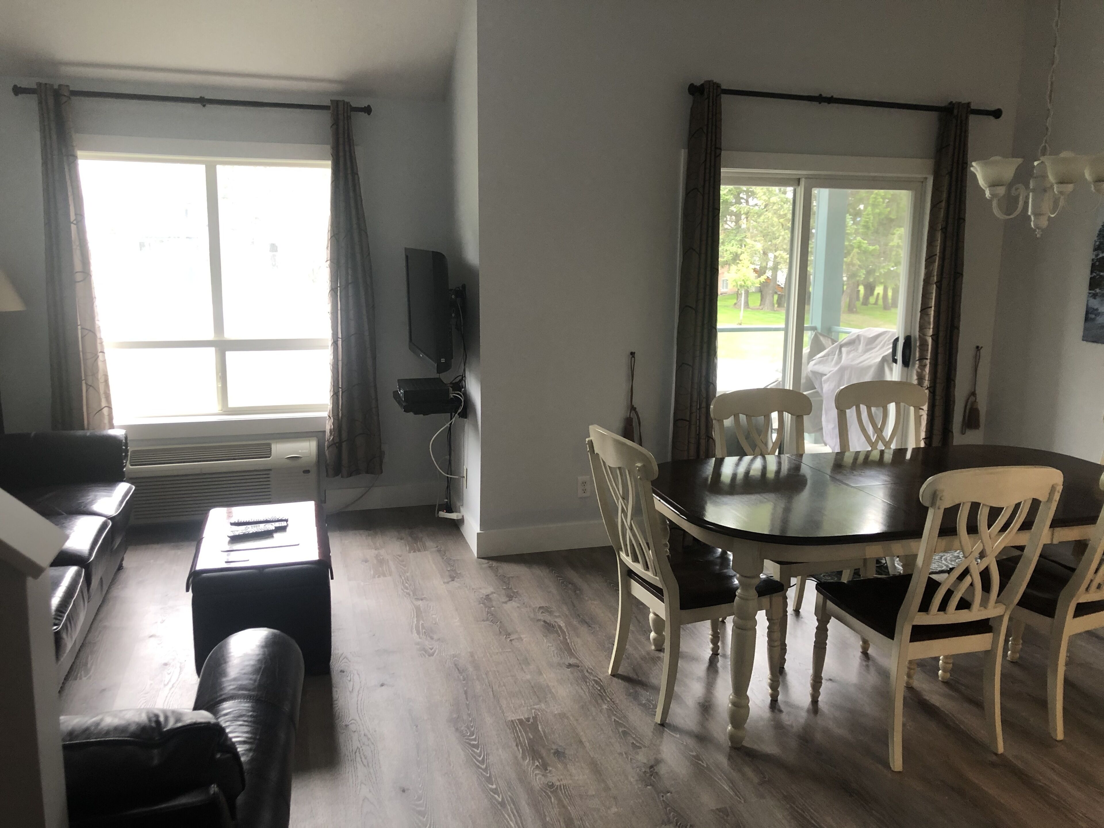 Un coin repas avec une table et des chaises, un téléviseur fixé au mur et une fenêtre avec des rideaux.