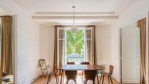 A dining room with a wooden table, six chairs, and a large window with curtains.