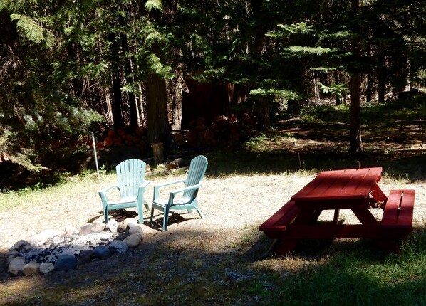 Un área de picnic con dos sillas Adirondack y una mesa roja en un entorno boscoso.