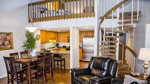 A spacious living area with a dining table, chairs, a leather sofa, and a staircase.