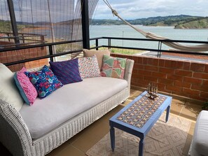 Ein Balkon mit einem Korbsessel, gemusterten Kissen, einem blauen Tisch und einer Hängematte.