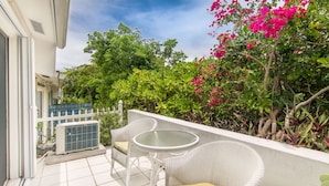Un balcon agrémenté de meubles en osier blanc, d’une table en verre et offrant une vue sur une végétation luxuriante et des fleurs roses.