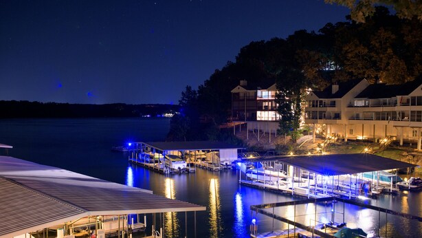 A marina at night with docked boats, a covered area, and buildings with illuminated windows.