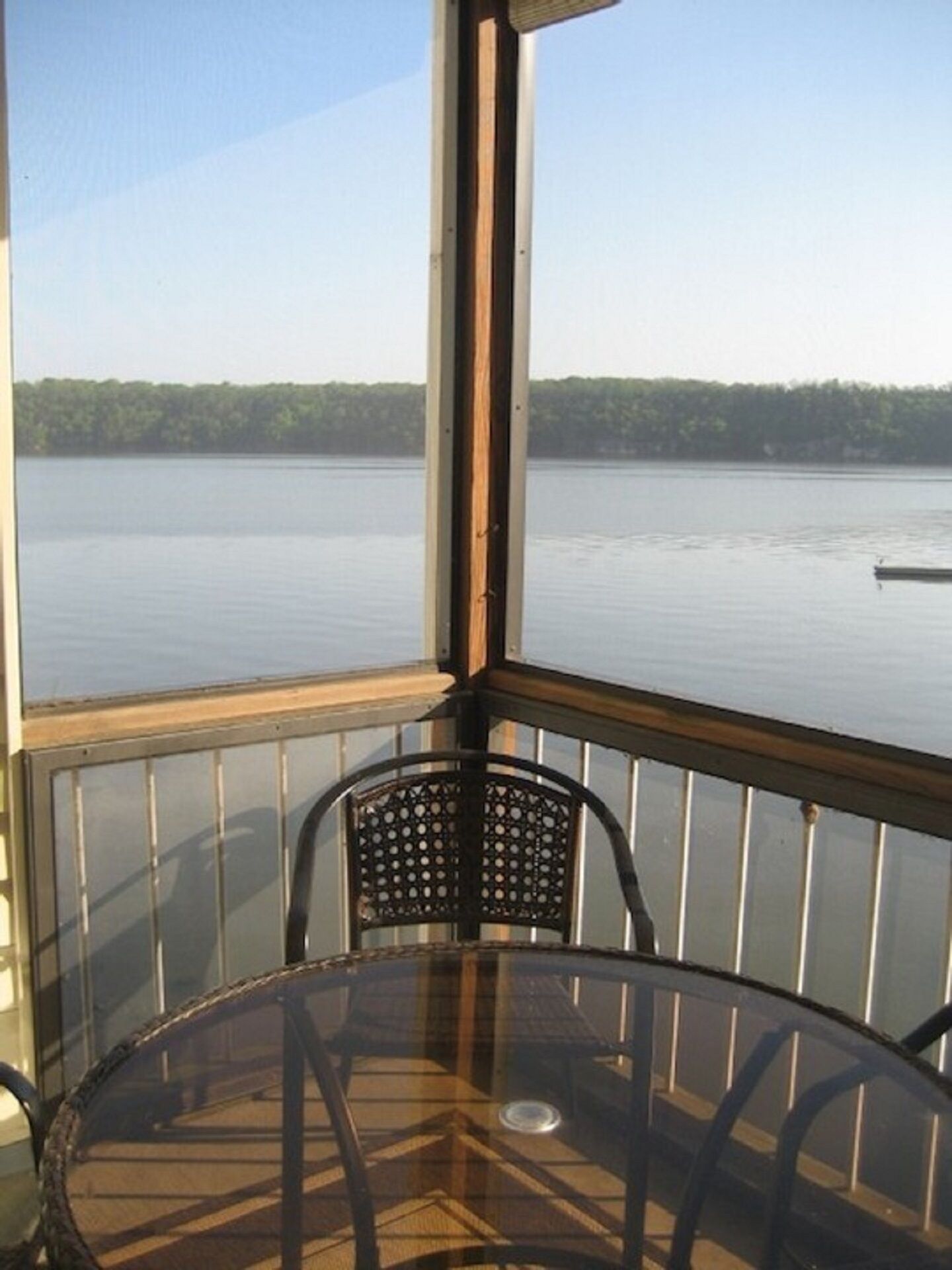 A corner of a room with a glass table and chairs, overlooking a calm lake with a dock in the distance.