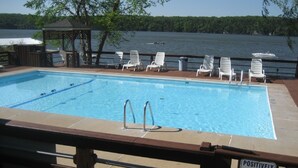 A rectangular pool with a wooden deck and lounge chairs. A sign states "Positively No Glass Allowed in Pool Area."