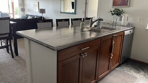 A modern kitchen with a central island, wooden cabinets, a built-in dishwasher, and a dining area with a sofa and chairs.