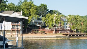 A lakeside property with a dock, a covered seating area, and a bridge leading to a building with multiple balconies and a sign reading "Breakwater Bay Club".