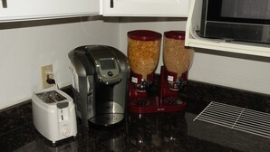 Et køkken med en brødrister, kaffemaskine og to beholdere med madvarer.