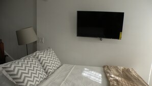 Et hotelværelse med en seng, et fjernsyn monteret på væggen og en lampe på et natbord.