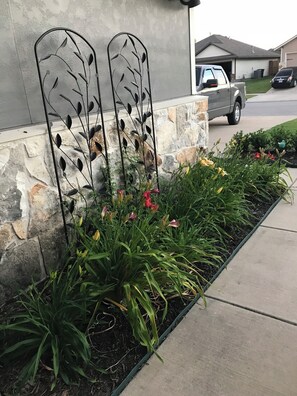 A landscaped garden bed with various plants and flowers, a stone wall, and a metal decorative fence.
