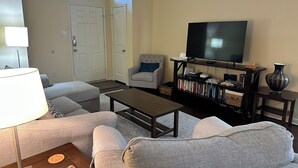 Ein Wohnzimmer mit Sofa, Couchtisch, Fernseher, Bücherregal und einer Lampe.