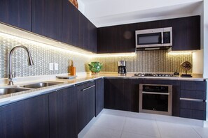 Une cuisine moderne avec des meubles de rangement aux couleurs sombres, un évier en acier inoxydable, un four à micro-ondes et un four encastré.